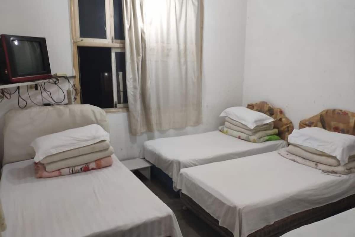 Una habitación con tres camas individuales, un televisor en un estante y una ventana con cortinas.