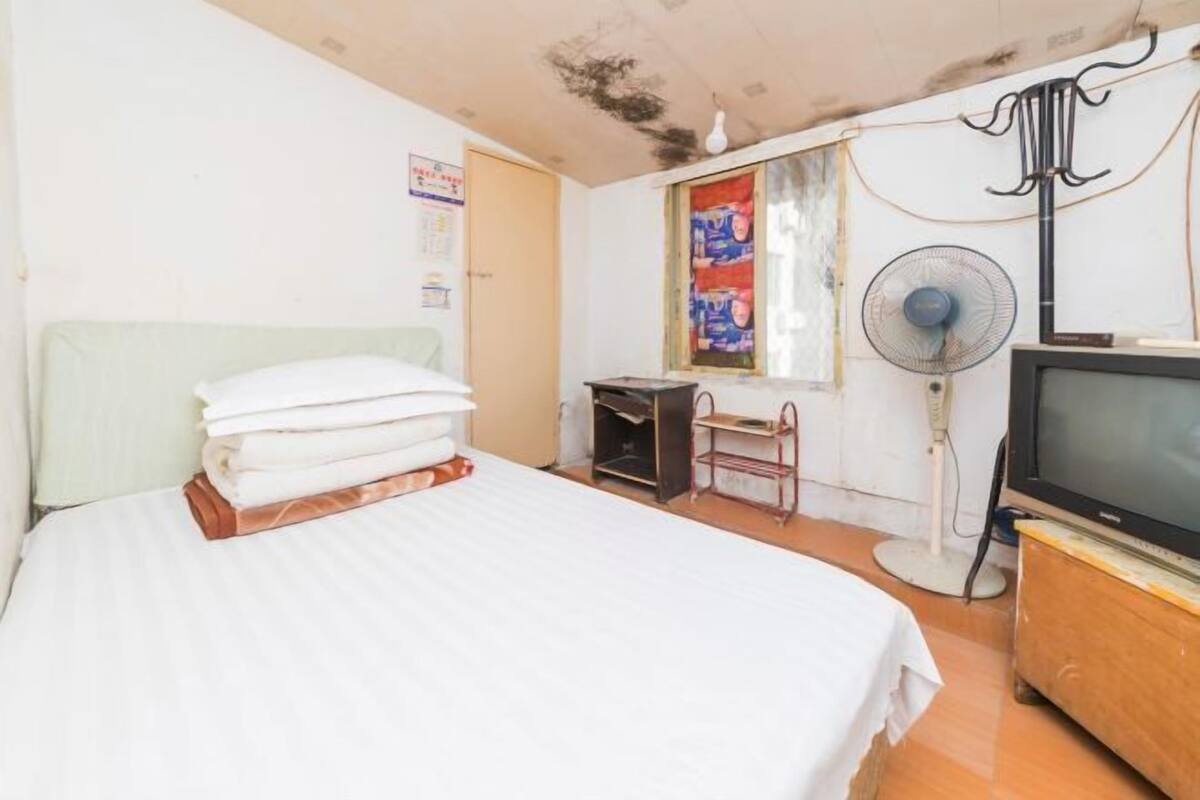 Habitación de hotel con cama, escritorio, silla, televisor y ventilador.