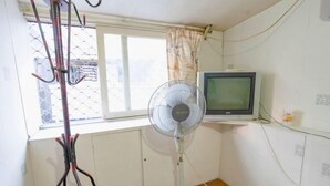 A room with a standing fan, a television on a shelf, and a window with curtains. - Yueqing Xinli Hotel (Yueqing)