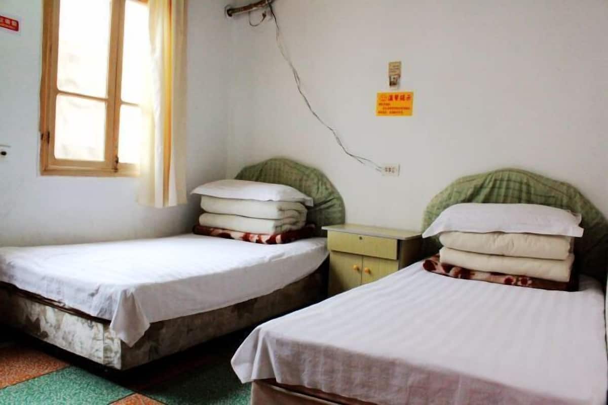 Dos camas individuales con sábanas blancas, una mesita y una ventana con cortinas.