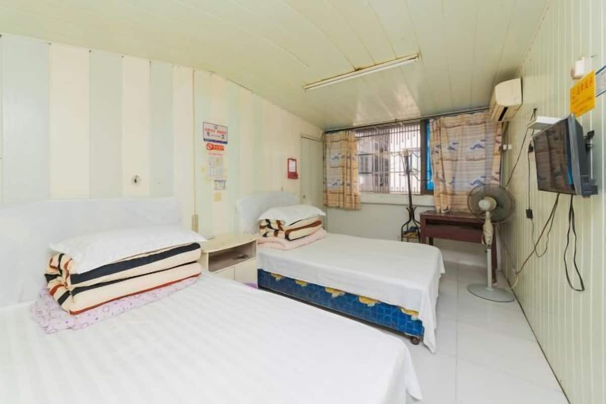 Una habitación con dos camas, un escritorio, una silla, un ventilador y una televisión.