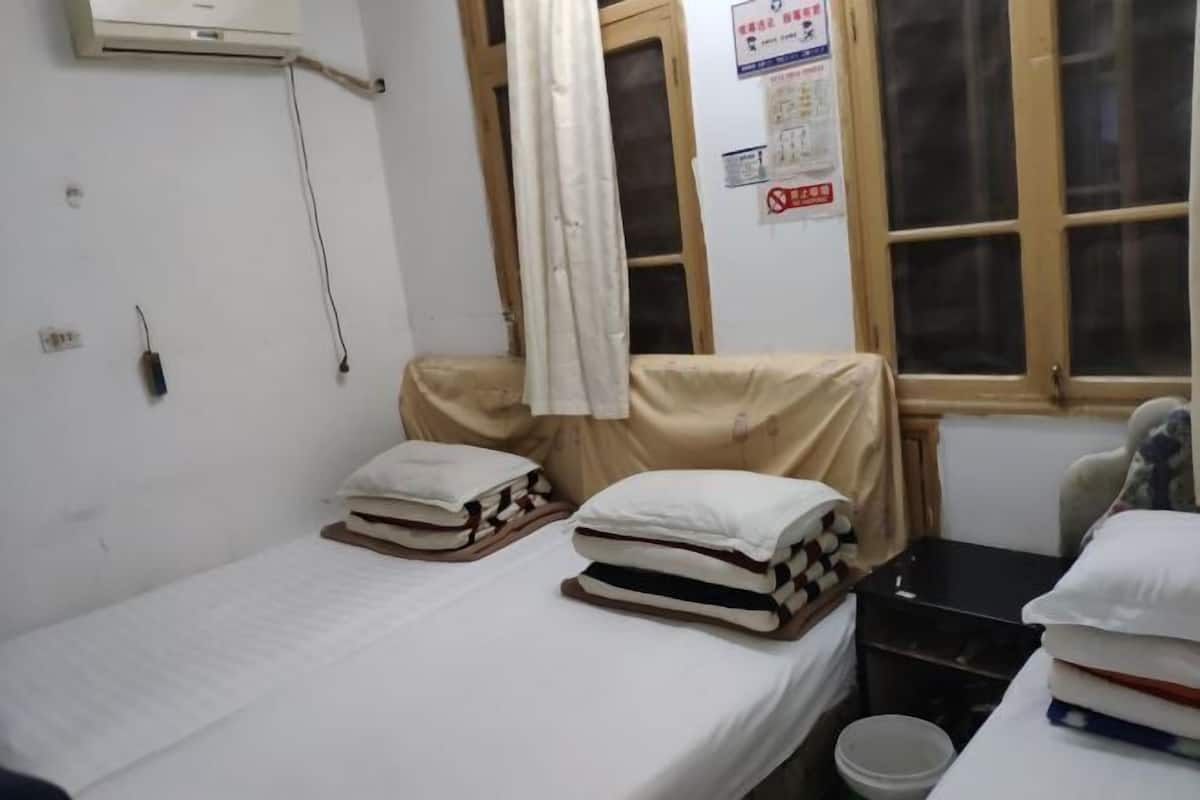 Una habitación pequeña y sencilla con una cama, una ventana, un radiador y aire acondicionado instalado en la pared.