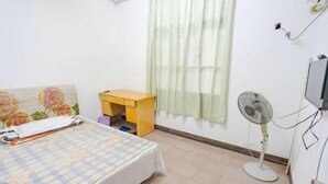 A bedroom with a bed, a small wooden nightstand, a standing fan, and a window with sheer curtains. - Yueqing Xinli Hotel (Yueqing)