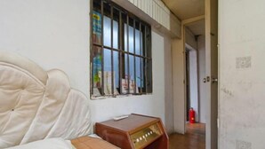 A room with a bed, a small wooden nightstand, a window with bars, and a door leading to another room. - Yueqing Xinli Hotel (Yueqing)