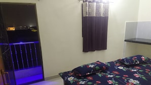 A room with a bed, a window with curtains, a door, and a small shelf. - Ajay Palace Home Stay (Faizabad)