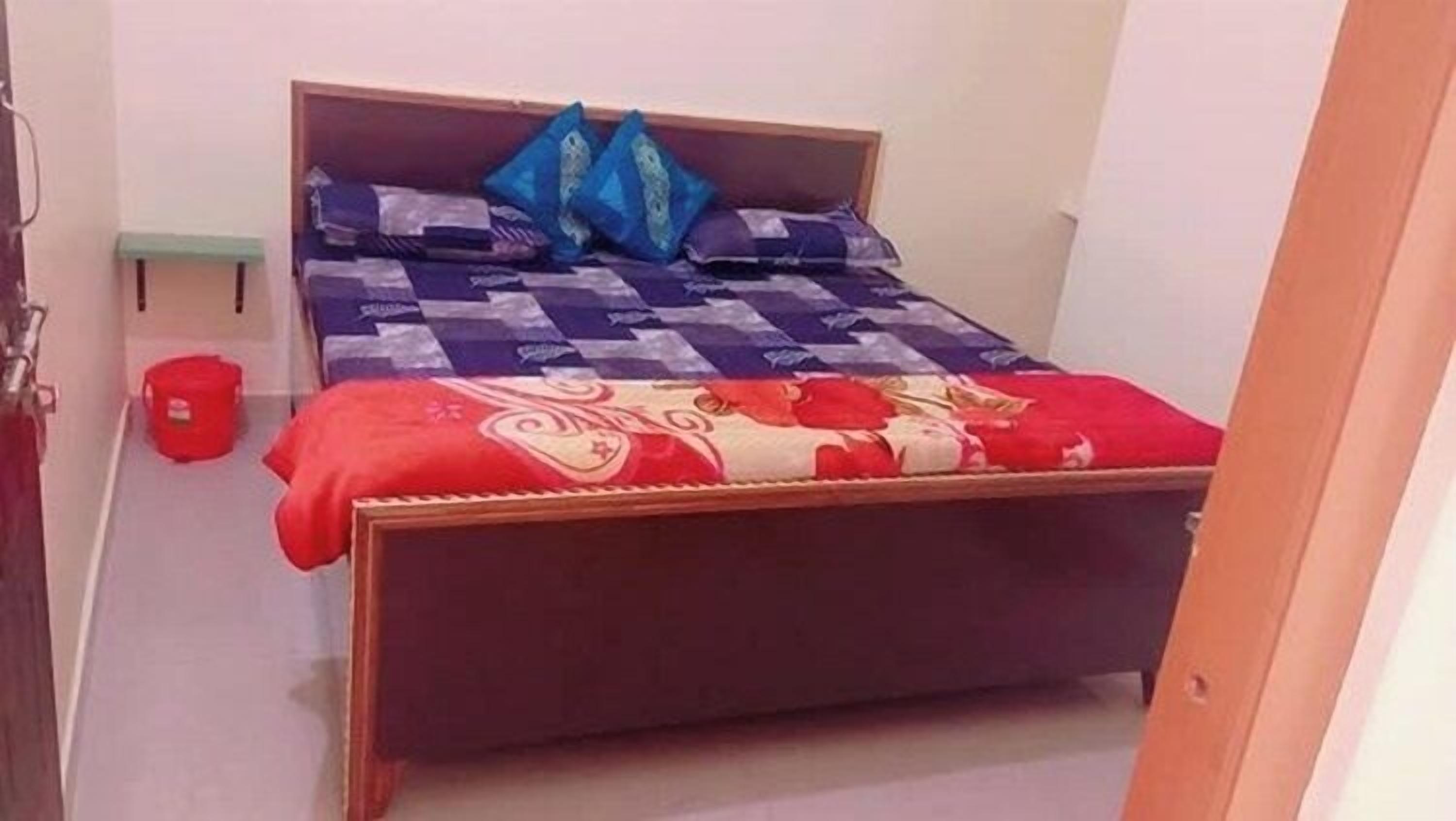 A bedroom with a wooden bed, a red and white patterned bedspread, and blue pillows.