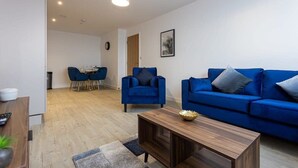 Ein modernes Wohnzimmer mit einem blauen Sofa, einem Holztisch und einer Essecke mit Tisch und Stühlen.