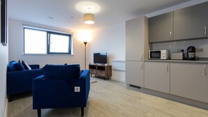Ein modernes Wohnzimmer mit einem blauen Sofa, einem Fernseher und einer Küchenzeile mit Schränken und Geräten.