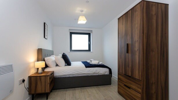 Ein Schlafzimmer mit Bett, Nachttischlampe, Kleiderschrank und Fenster.