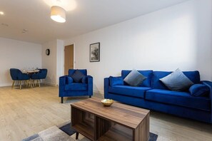 Una sala de estar moderna con un sofá azul, una mesa de centro de madera y una zona de comedor con una mesa pequeña y sillas.