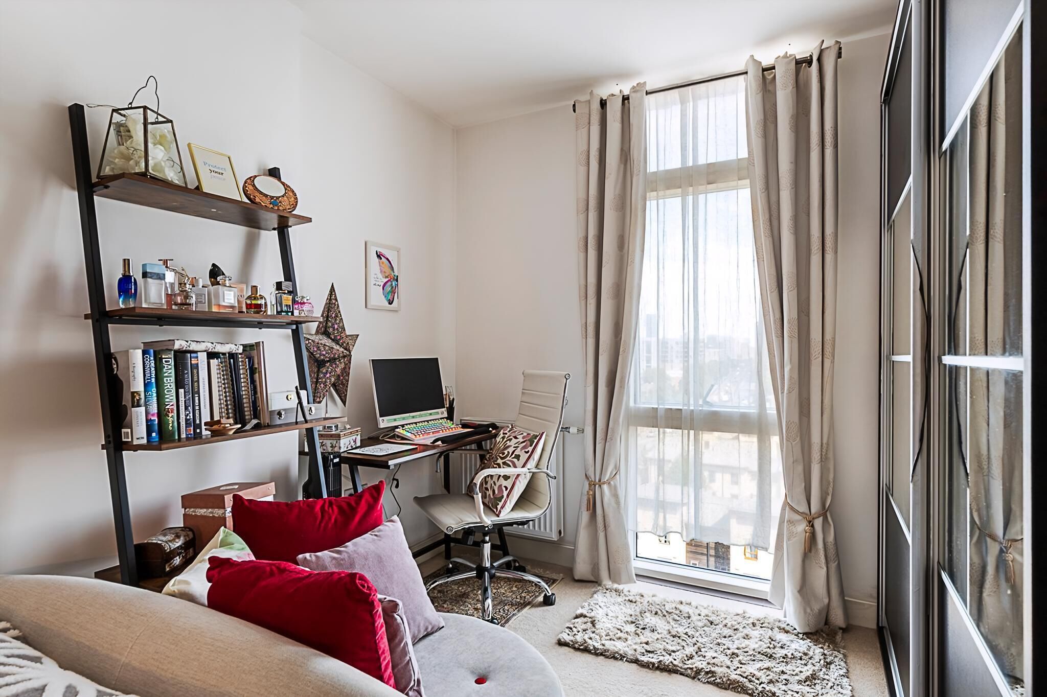 Ein modernes Schlafzimmer mit Bett, Schreibtisch inklusive Computer, Bücherregal und einem Fenster mit Vorhängen.
