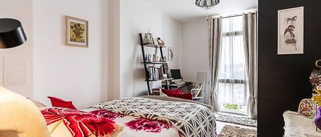 A bedroom with a bed, a desk, a chair, a bookshelf, and a window with curtains.