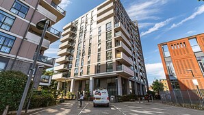 Un edificio residenziale a più piani con balconi, un'area di parcheggio e un furgone bianco parcheggiato di fronte.