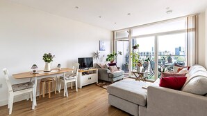 Un soggiorno moderno con zona pranzo, un divano grigio, una TV e ampie finestre con vista sulla città.