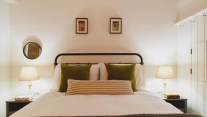 A neatly made bed with a striped pillow, two green pillows, and a dark throw blanket. There are two bedside lamps on either side of the bed. - Seaside Escape Cottage in Broadstairs (Broadstairs)