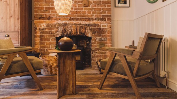 A cozy room with a brick fireplace, two wooden chairs, a woven basket, and a hanging light fixture. - Seaside Escape Cottage in Broadstairs (Broadstairs)