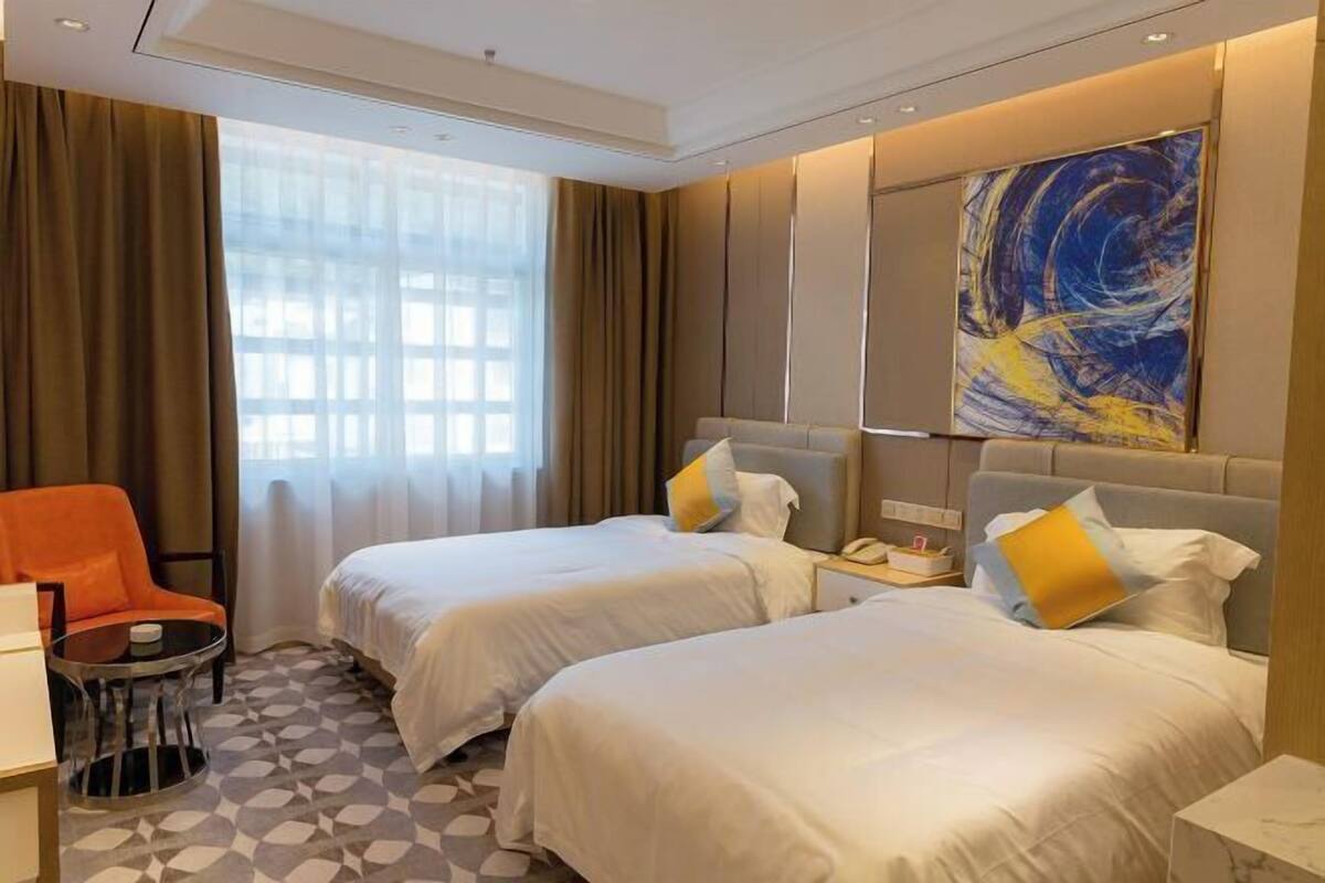 Ein Hotelzimmer mit zwei Betten, einem Schreibtisch, einem Stuhl, einem Fenster mit Vorhängen und einem großen abstrakten Gemälde an der Wand.