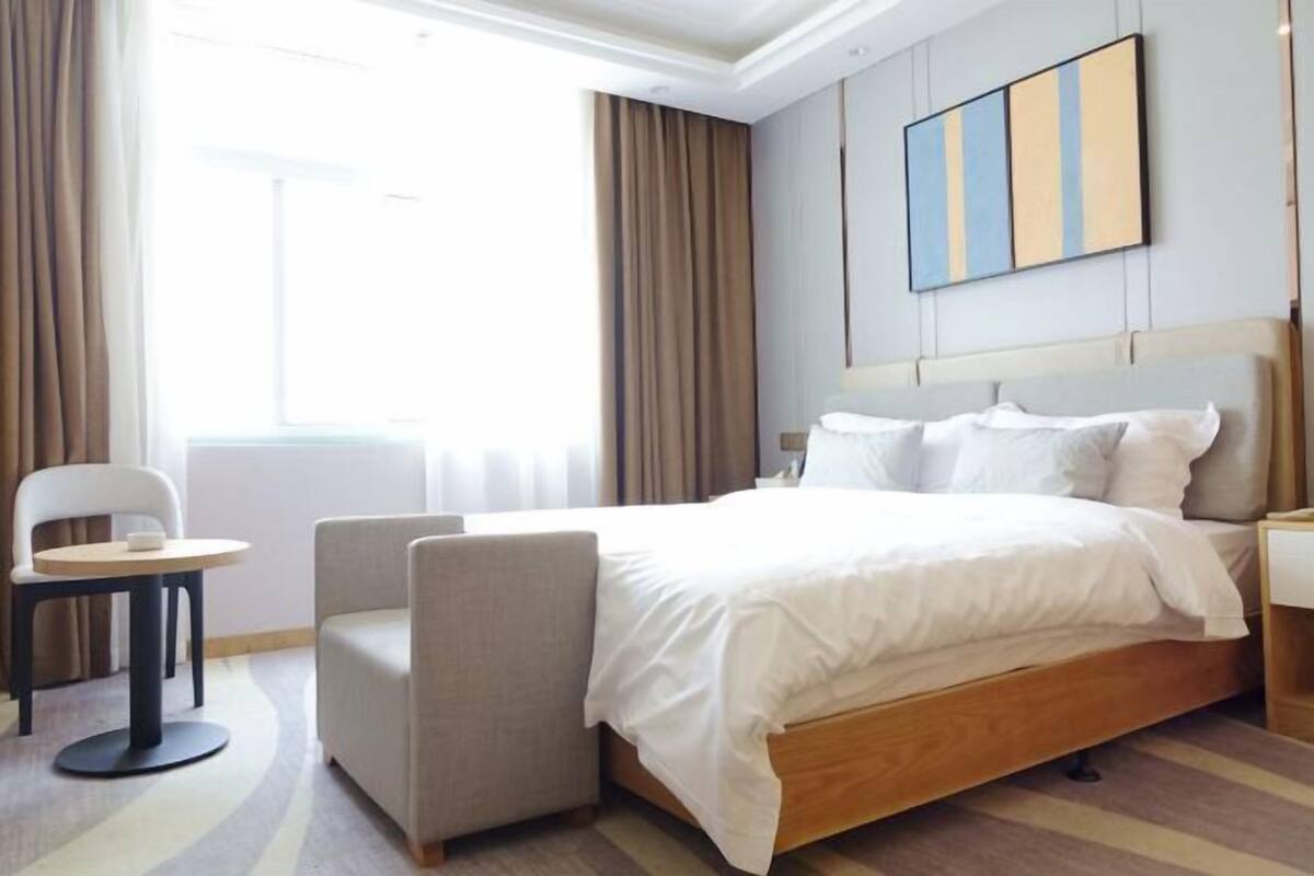 Ein Hotelzimmer mit Bett, Sessel, kleinem Tisch und einem Gemälde an der Wand.