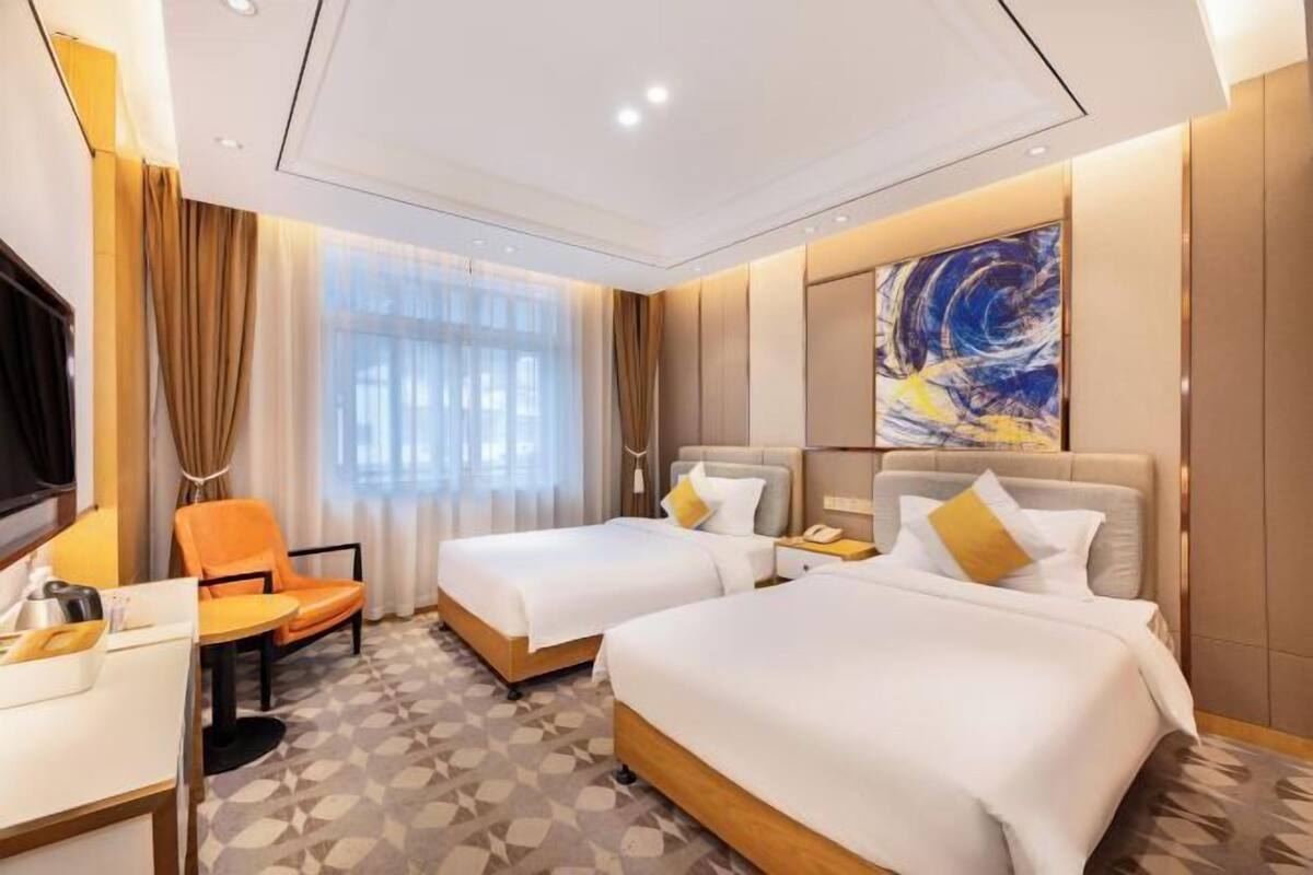 Ein Hotelzimmer mit zwei Betten, einem Schreibtisch, einem Stuhl und einem großen, abstrakten Gemälde an der Wand.