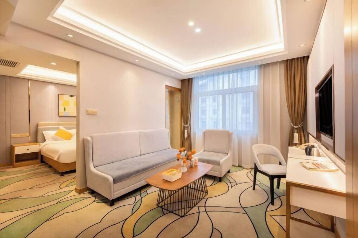 Ein modernes Hotelzimmer mit Sofa, Ohrensessel, Schreibtisch und einem großen Fenster mit Vorhängen.