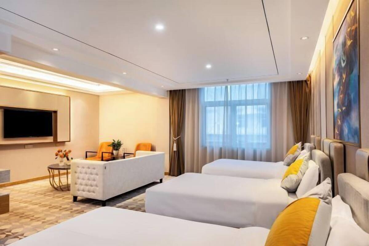 Ein Hotelzimmer mit zwei Betten, einem Sofa, einem Fernseher und einem großen Fenster mit Vorhängen.