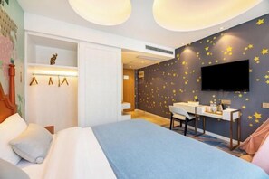 Une chambre d’hôtel équipée d’un lit, d’un bureau, d’une chaise, d’un téléviseur à écran plat et d’un mur décoré d’autocollants en forme d’étoiles.