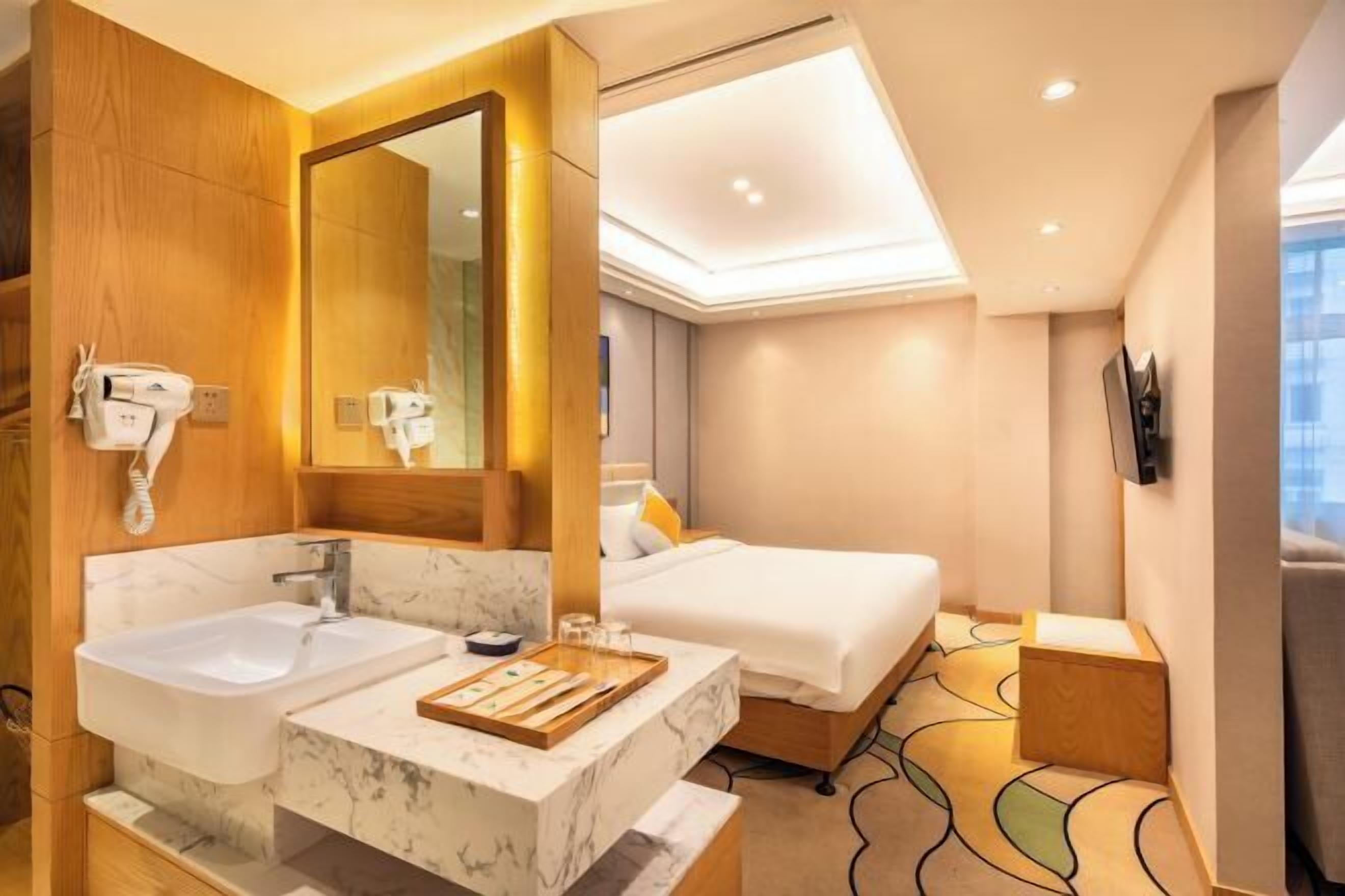 A hotel room with a double sink, a large mirror, a bed, and a TV mounted on the wall.