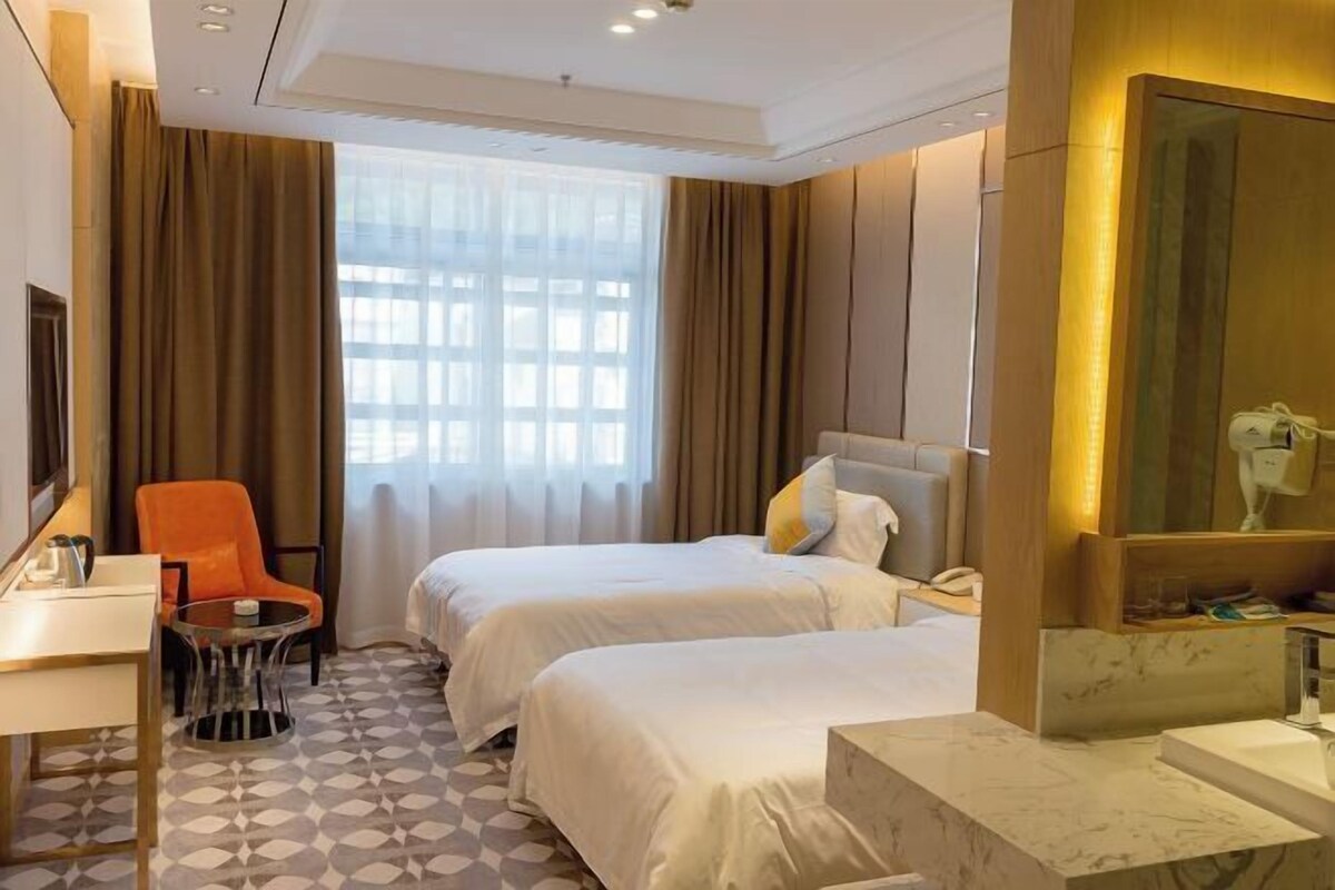 Une chambre d’hôtel avec deux lits, un bureau, une chaise, une petite table et une salle de bain équipée d’un miroir et d’un lavabo.