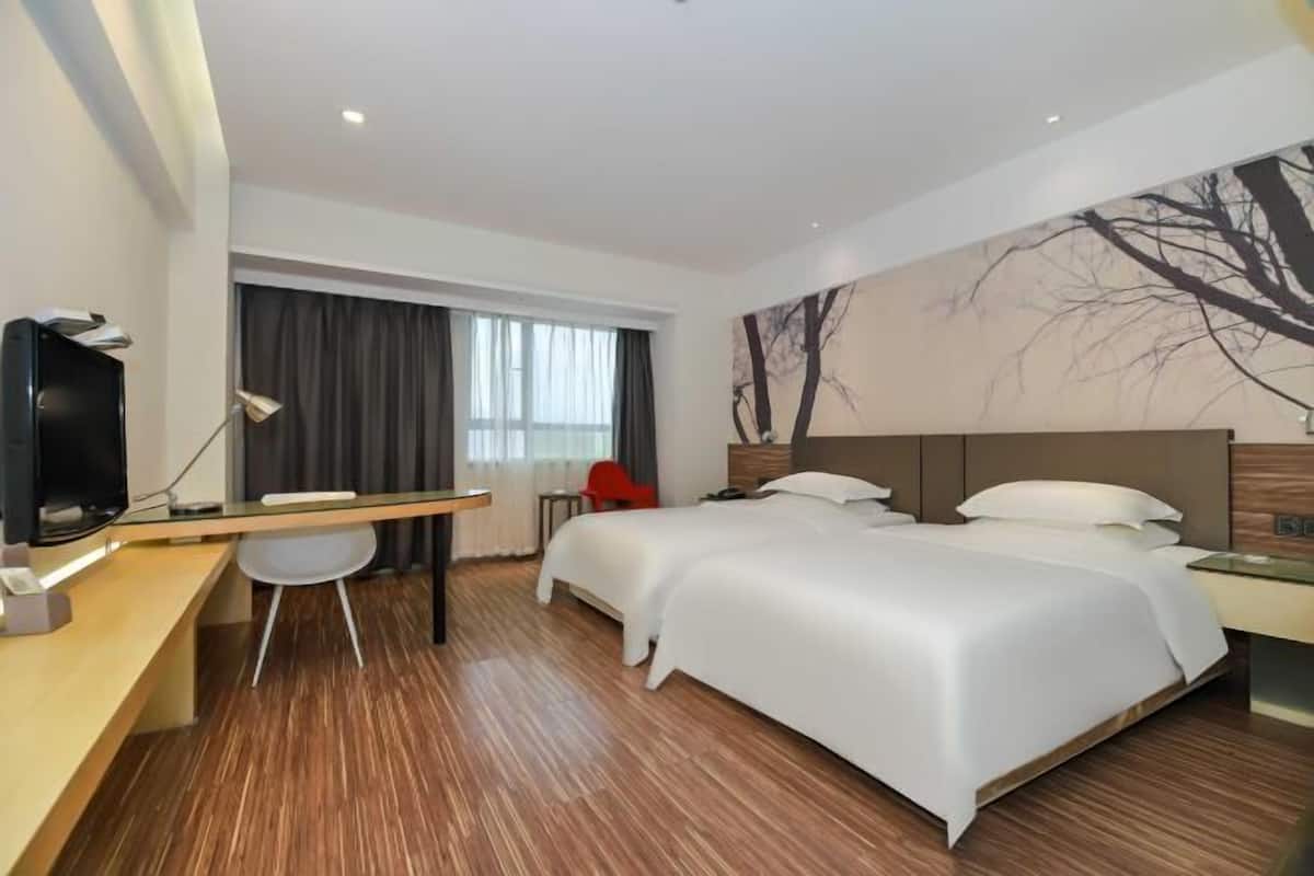 Une chambre d’hôtel avec un lit, un bureau avec un ordinateur, une chaise, une télévision et une fenêtre avec des rideaux.