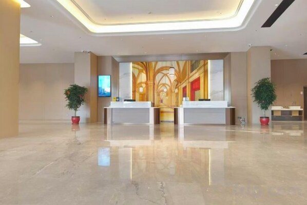 A hotel reception area with two reception desks, a large wall mural, and potted plants.