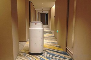 Un couloir d’hôtel avec une poubelle, un sol recouvert de moquette et des portes de chaque côté.