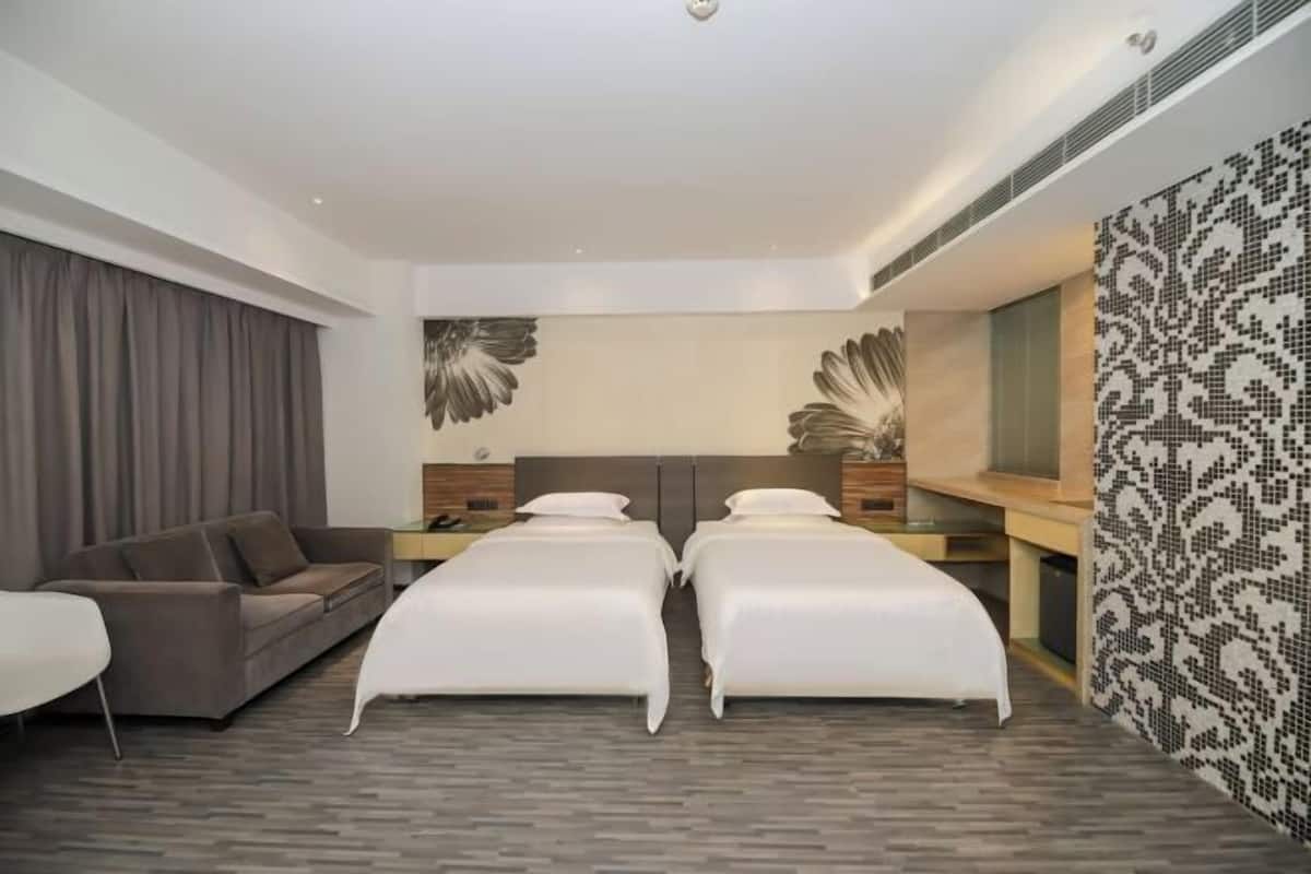 Une chambre d’hôtel moderne équipée de deux lits simples, d’un canapé, d’un bureau et d’un grand miroir.