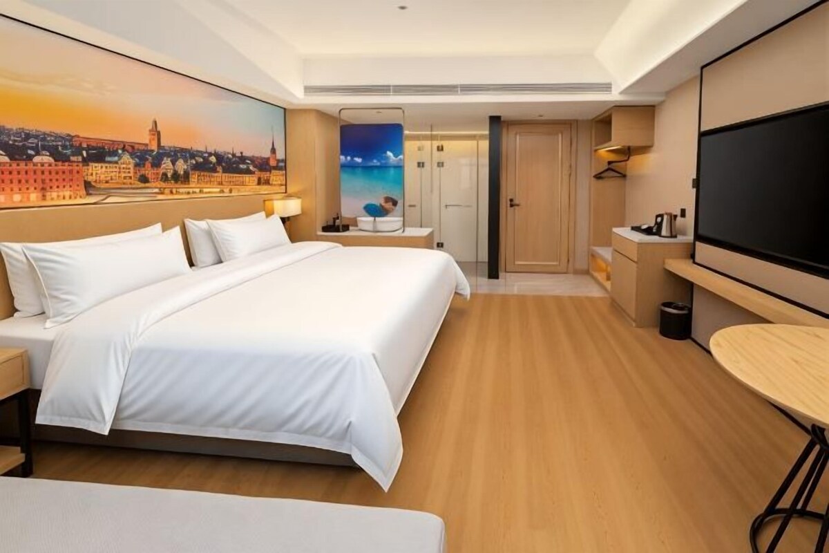 A hotel room with a large bed, a desk, a chair, a TV, and a painting on the wall.