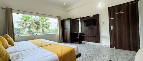 A hotel room with a bed, a TV, a wardrobe, and a balcony with a view of palm trees.