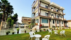 A modern multi-story building with a balcony, potted plants, and outdoor seating. - Hotel Vrinda Sarovar (Mathura)