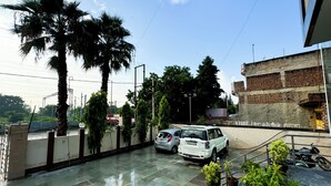A parking area with two cars, a palm tree, and a building with a brick facade. - Hotel Vrinda Sarovar (Mathura)
