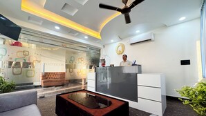 A modern hotel lobby with a reception desk, a sofa, a coffee table, and a ceiling fan. - Hotel Vrinda Sarovar (Mathura)