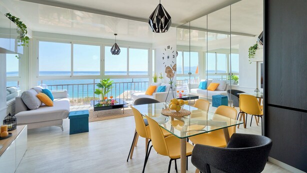 A modern living room with a glass table, yellow chairs, and a view of the sea.