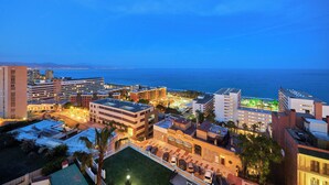 A hotel complex with multiple buildings, a parking area, and a view of the sea.
