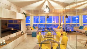 A modern living room with a glass dining table, yellow chairs, and a large flat-screen TV.