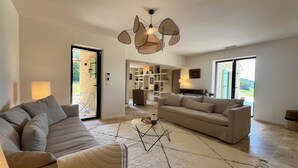A spacious living room with a large sofa set, a coffee table, and a unique hanging light fixture. There is a door leading to a balcony with a view of the outdoors. - LE Mas Jas, magnificent Mas Provençal - Lauris (Lauris)