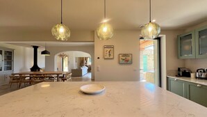 A spacious kitchen with a large island, pendant lights, and a view into the dining area. - LE Mas Jas, magnificent Mas Provençal - Lauris (Lauris)