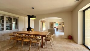 A spacious dining area with a wooden table and wicker chairs, a black pendant light, and a view into a living area with a staircase. - LE Mas Jas, magnificent Mas Provençal - Lauris (Lauris)