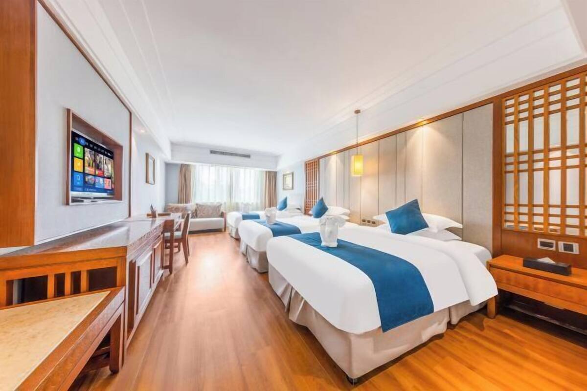 A hotel room with three beds, a wooden desk, and a TV on the wall.