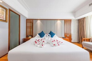 Une chambre d’hôtel avec un lit bien fait, une tête de lit en bois, une table de chevet avec une lampe et une vue sur l’extérieur par une fenêtre.