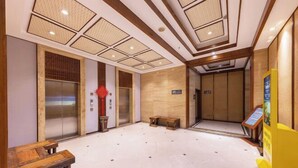 Un vestíbulo de hotel con un banco de madera, dos ascensores, un mostrador de recepción y piso de baldosas.
