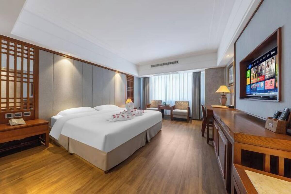 A hotel room with a large bed, a desk, a TV, and a seating area.