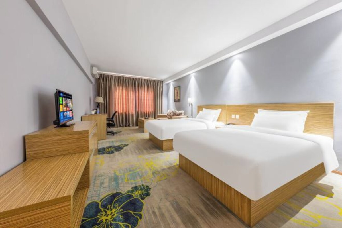Una habitación de hotel con dos camas, un escritorio, un televisor y una ventana con cortinas.