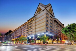 Un hotel de varios pisos con un diseño de esquina destacado, un paso de peatones y diversas tiendas a lo largo de la calle.