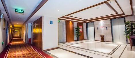 A hotel corridor with a red carpet, a reception area, and a large mirror.
